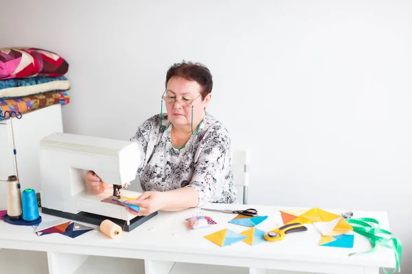 Συνονθύλευμα και quilting στο εργαστήριο ένας ράφτης γυναίκα σε άσπρο φόντο - ράφτης χέρια ράβω σε ράβοντας μηχανή αποκόμματα από μπλε και κίτρινο ύφασμα για μωσαϊκό. — Φωτογραφία Αρχείου