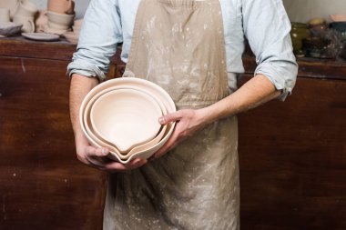 çanak çömlek, araçlar, Seramik Sanat kavramı - pişmiş kaseler, şirin bitmiş kil mutfak eşyaları, ahşap yüzey arka plan ile işyerinde erkek ustası ellerinde yakın çekim.