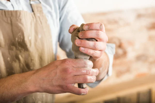 Poterie, grès, céramique concept d'art - gros plan sur les mains de maître tenant un morceau d'argile chaude, jeune homme dans le travail de tablier sale dans un atelier, les mains des hommes forment le futur produit de l'argile brute . — Photo