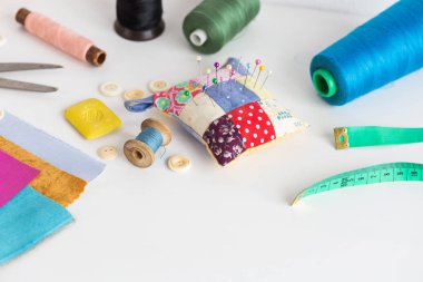 dikiş araçları, patchwork, terzilik ve moda kavramı - studio, iğnelik, iş parçacığı makaralar, ölçme metre, düğmeler, makas, sabun, renkli patchwork kumaş parçaları beyaz masa üzerinde yakın çekim.