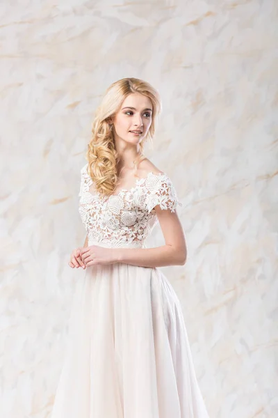 Vestido de novia de moda, hermoso modelo rubio, peinado de novia y concepto de maquillaje - mujer joven romántica en vestido blanco de lujo en el interior sobre fondo claro, posando mujer perfecta en el estudio . — Foto de Stock