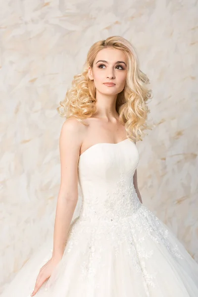 Vestido blanco de moda, hermosa modelo rubia, peinado de novia y el concepto de maquillaje - chica joven soñando en vestido de fiesta de boda, de pie en el interior sobre fondo claro, mujer esbelta romántica posando . — Foto de Stock