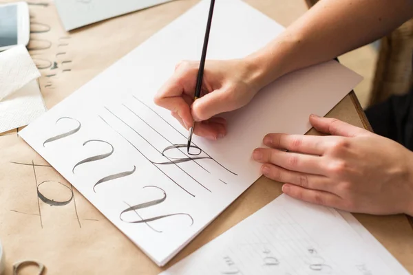 Tekenen, talent, praktijk concept. over het dunne Witboek voor kopieerapparaten en printers jonge vrouw met nette manicure schilderij initiaal met enige tip van het penseel — Stockfoto