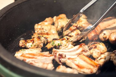 et yemek tarifleri, gıda ve piknik kavramı - portre üzerinde bir özel ızgara tava açık havada yemek bile metal mutfak maşa tarafından yemek pişirmek için dönüm güneşli gün, kavrulmuş domuz pirzolası lezzetli sulu parçalar üzerinde.