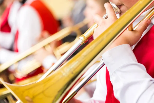 Instrumento musical, banda de bronze e conceito de celebração - close-up tocando trombone com bocal e mãos masculinas, desempenho de férias de músicos em ternos de concerto vermelhos e brancos, foco seletivo . — Fotografia de Stock