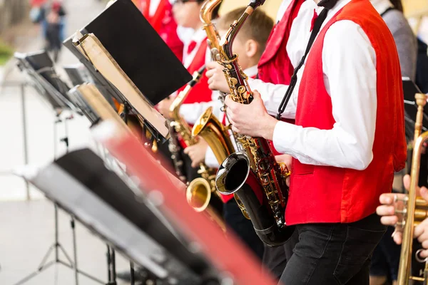 musical instrument, brass band and orchestra concept - festive performance of saxophones, closeup on sax and sheet music stands, musicians in red concert jackets and shirts, selective focus.