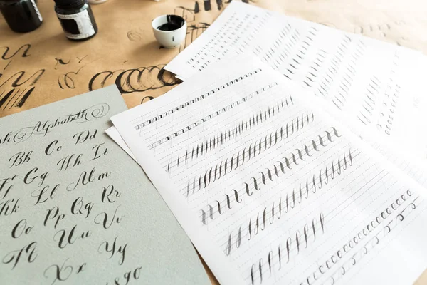 Calligraphy, education, graphic design concept. lots of exercises for training skills of calligraphy with help of special supplies like black ink, brushes and white lined sheets — Stock Photo, Image