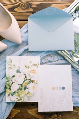 Aksesuar, evlilik, hassasiyet kavramı. pastel tonları muhteşem flatlay. hafif mavi bir zarf içerisinde mektup, iki posta kartları ile çiçek tasarım var. Üç altın yüzük ve gelinin yumuşak pembe Ayakkabı