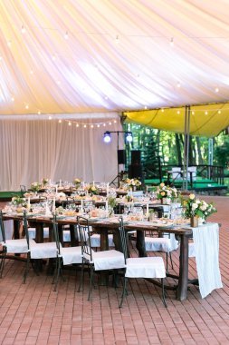 kutlama, lokanta işi, Düzen çok kavramı. kahverengi ahşap tablolarla ayarı derli toplu ve büyük çadır altında duran ve misafirler için bekleyen Çiçek demetleri zengin