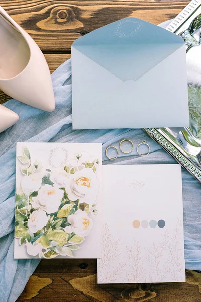 Accessoire, nuptial, tederheid concept. prachtige flatlay van pasteltinten. Er is een licht blauwe envelop brief, twee postkaarten met bloemmotief. drie gouden ringen en zachte roze schoenen voor de bruid — Stockfoto