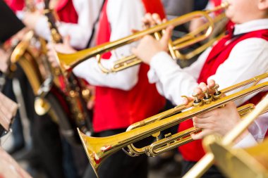 jazz band performance concept - orchestra of wind instruments during the variety show, selective focus on hands of musicians playing on trumpets and saxophones, closeup male in red concert costumes. clipart