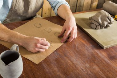 çanak çömlek üretimi, esnaf araçları, Seramik Sanat kavramı - üstten görünüm genç adamın toprak çizim üzerinde çalışan el, bir Fransız giymiş bir gömlek ve Resepsiyon ve bitmiş sürahi arkasında oturan önlük.