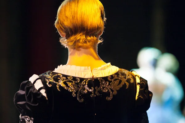 performance, illumination, theater concept. back of the head of man in gorgeous costume of prince, in light of projector his blond hair becomming rich gold shades