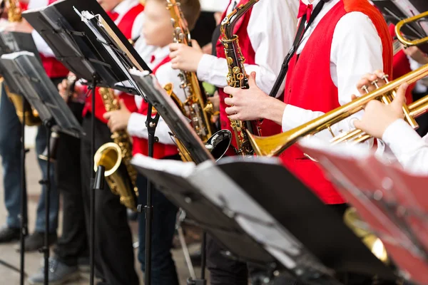 Instrumento musical, banda de bronze e conceito orquestra - conjunto close-up de músicos tocando trompete e saxofone em trajes de concerto vermelho, suporte de música, mãos masculinas com equipamentos, foco seletivo . — Fotografia de Stock