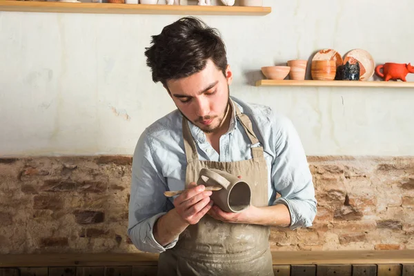 Potter, atölye, Seramik Sanat kavramı - duran genç bir önlük, erkek eller kil Kupası ve aracı, bir Fransız işyerinde ham ürün ile esmer adam giymiş.