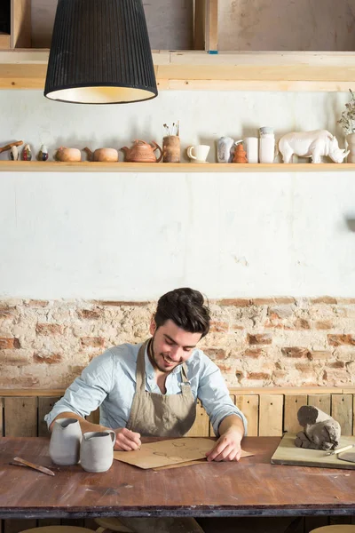 Potter, esnaf araçları, Seramik Sanat kavramı - genç erkek planlanan toprak karakalem ile çalışma, ana tasarım çizer ve gelecekteki ürünler, önden görünüm, dikey boyutlarda giderir.