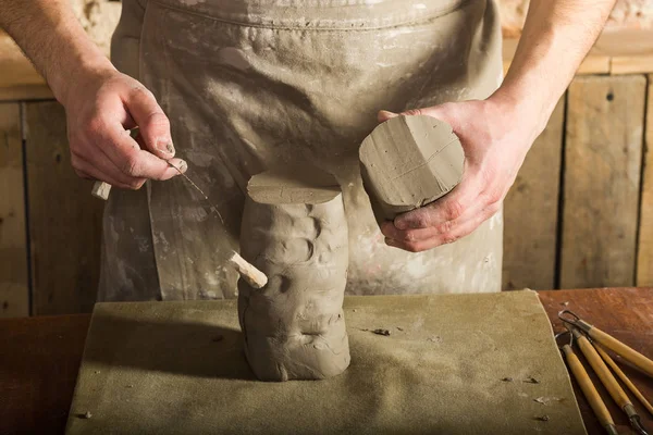 potter, clay workshop, ceramics art concept - close-up on hands of male ceramist, standing man cut off the part of raw fireclay with the string cutter, wooden table with sculpting tools set.