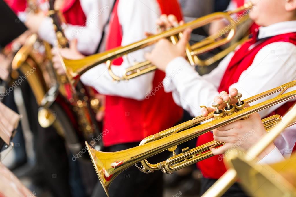 jazz band performance concept - orchestra of wind instruments during the variety show, selective focus on hands of musicians playing on trumpets and saxophones, closeup male in red concert costumes.