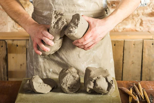 Potter, araçlar, Seramik Sanat kavramı - makro görünümü şamot, erkek bir önlük, bir Fransız masada hammadde ile giyinmiş büyük parçalarını tutan genç ustanın ellerinde.