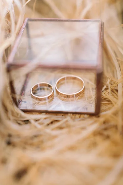 Joyería, ceremonia de compromiso, concepto de tradiciones. en la pequeña caja de vidrio colocada en la paja para la seguridad hay dos anillos de boda de oro en forma simple de estilo minimalista — Foto de Stock