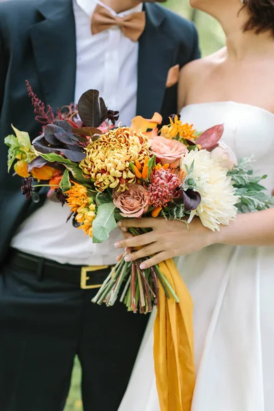 relationships, celebrating, fall concept. there is wonderful couple of lovers, bride and fiance, dressed in modern wedding costumes with big bunch of delicate flowers strapped with sunny yellow ribbon