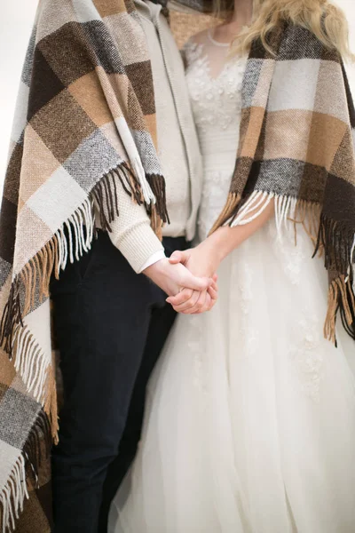 Amor, compromiso, concepto de atmósfera. hay una dulce pareja de recién casados vestidos con trajes de novia y envueltos en cómodos cuadros con flecos, se toman de la mano el uno al otro — Foto de Stock