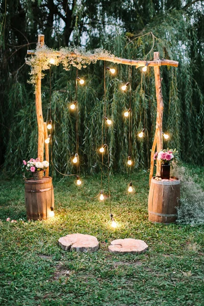 Verlobungszeremonie, Liebe, Designkonzept. in der Dämmerung gibt es atemberaubende Hochzeitsbogen im rustikalen Stil mit funkelnden Lichtern und Sträußen aus verschiedenen Blumen dekoriert — Stockfoto