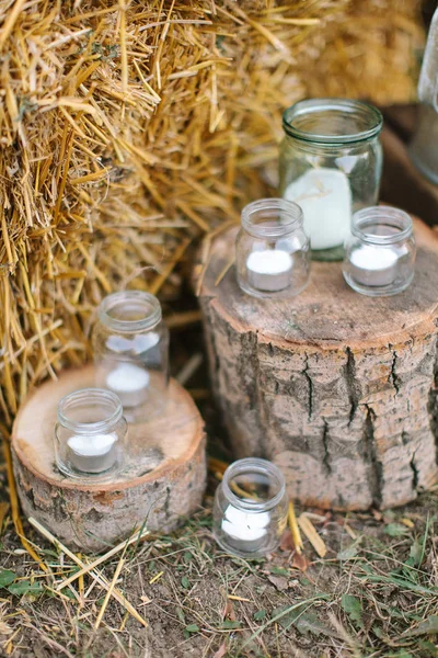 Diseño de fiesta, otoño, concepto de estilo país. frascos de vidrio brillante de diferentes tamaños utilizados como candelabros originales colocados en el suelo con heno y dos tocones de árboles de madera — Foto de Stock