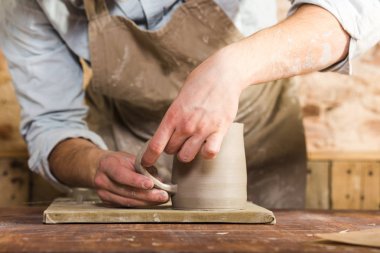 potter, taş, Seramik Sanat kavramı - bağlantı Kupası closeup usta eller ve ham kil, kil, parçaları ile ana parmak çalışır yapılmış erkek tanıtıcı bir atölye masanın arkasında duruyor.