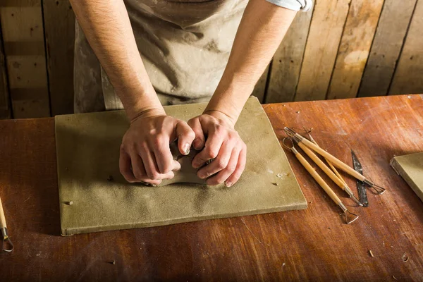 Ceramica, laboratorio, concetto di arte ceramica - primo piano su mani maschili che impastano la piastra, ceramista con materia prima su tavolo in legno con set di utensili da scultura, vista dall'alto . — Foto Stock