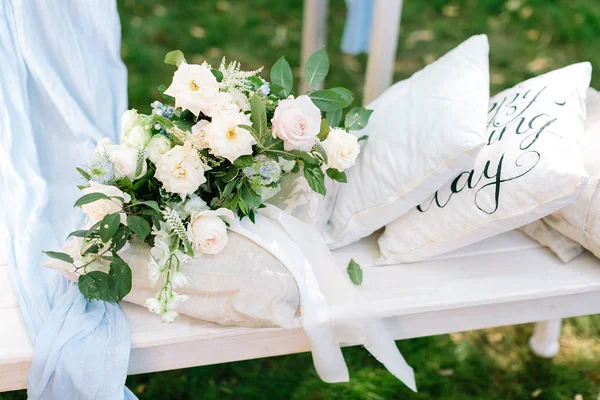 Gemak, romantiek interieurconcept. op witte tuin bankje is er een prachtig boeket van verschillende prachtige bloemen in de buurt van paar kussens van wit en beige kleur — Stockfoto