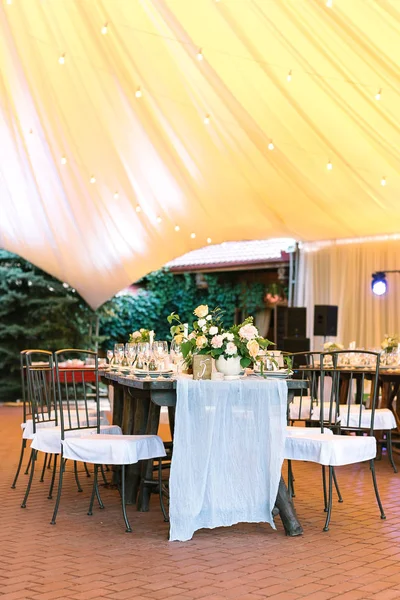 decoration, style, holidays concept. long wooden table created of smaller ones and comfortable chairs arranged under high big yellow tent for celebrating wedding day