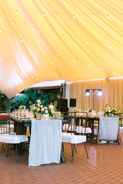 Illumination, célébration, concept de bonheur. restaurant sous grande tente jaune comme coucher de soleil préparé pour le banquet, toutes les tables sont servies avec des plats et des fleurs, et les projecteurs sont allumés — Photo