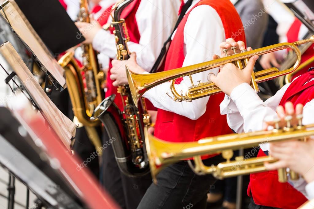 musical instrument, brass band and orchestra concept - closeup ensemble of musicians playing on trumpets and saxophones in red concert costumes, male hands with shiny equipment, selective focus.