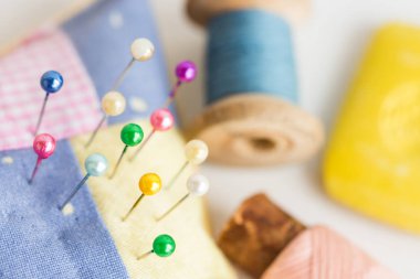 Dikiş, yorgan dikme, dikiş ve terzilik konsepti - renkli şirin dikişli iğneli iğne, beyaz masaya yakın aletler, mavi ve pembe iplik makaraları, seçici odak, üst görünüm.