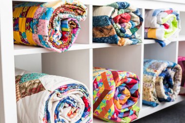 yama işi, dikiş ve moda konsepti - altı raflı beyaz kitaplık ve stüdyoda parlak tamamlanmış yorganlar, bitmiş ürünlerin deposu, yan görüş.