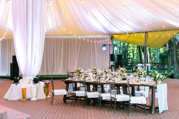 Performance, wedding, party concept. beautiful space for celebrating one of the most important event, marriage. there are served tables under large tent, yellow lights and bright projectors — Stock Photo, Image