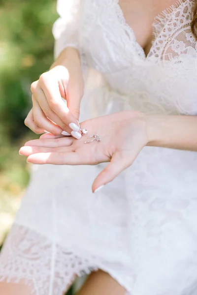 Närvarande, juvel, tillbehör koncept. ljushyad kvinna som bär vit klänning med snörning tar två vackra dizzling silver öra-ringar med klart genomskinligt diamanter skinande ljuset av solen — Stockfoto