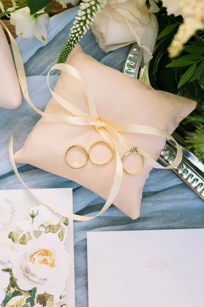 Present, surprise, wedding concept. nice top view of little peachy color pillow with thin ribbon, there is three golden rings on it, and nearby few postcards with painting of roses — Stock Photo, Image