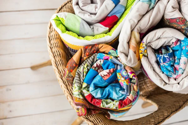 Patchwork and fashion concept - closeup on three beautiful quilts rolled into a tube and laid in a wicker chair, warehousing of finished products on a white background, top view, flat lay. — Stock Photo, Image