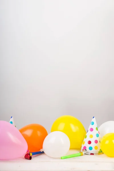 Feste, feste, celebrazioni. modello adorabile per compleanno o anniversario congratulazione, sulla superficie bianca del tavolo ci sono un sacco di palloncini, cappelli da festa e fischi. spazio libero per il testo — Foto Stock