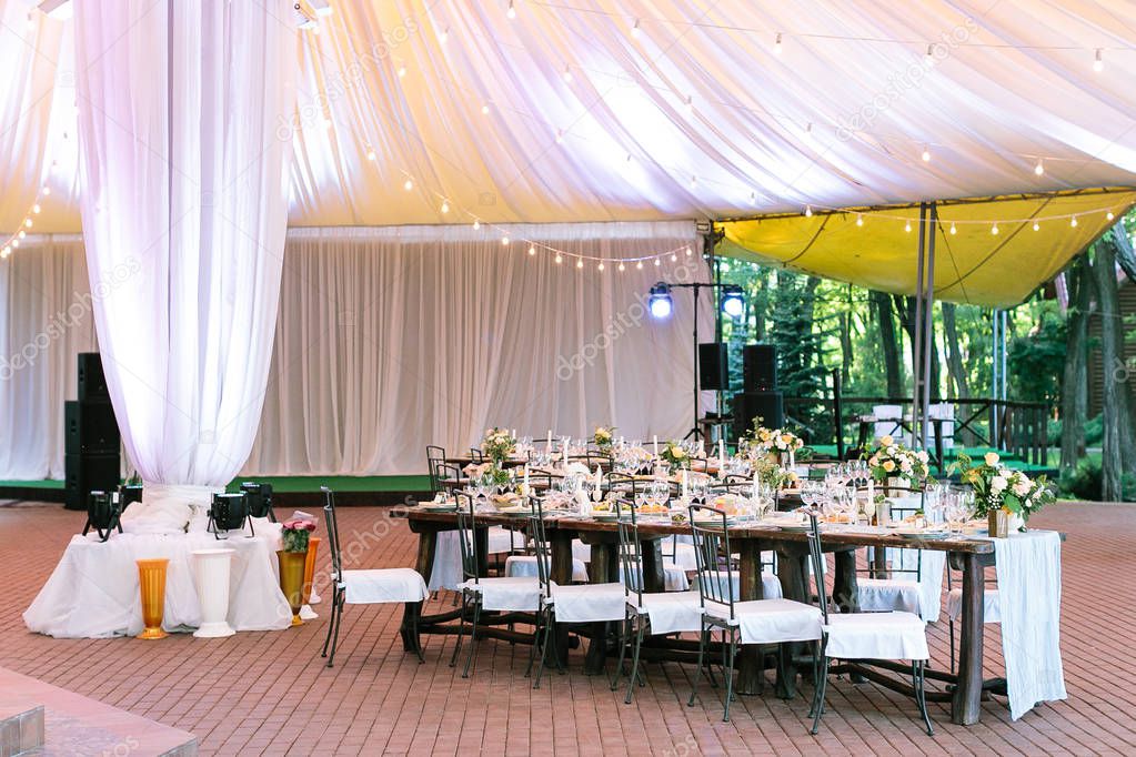 performance, wedding, party concept. beautiful space for celebrating one of the most important event, marriage. there are served tables under large tent, yellow lights and bright projectors