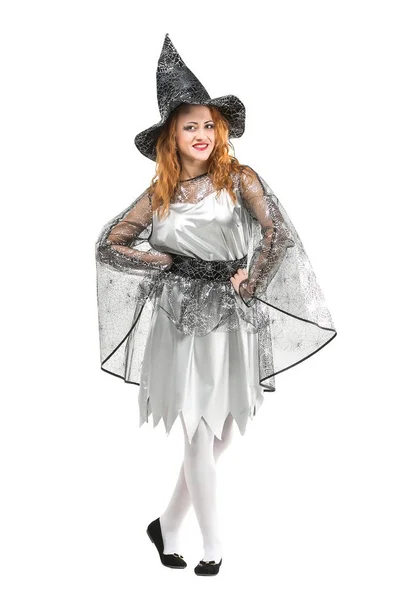 Halloween, mystic, holidays concept. isoalted red haired charming witch wearing pointy hat, silver dress with light shawl decorated with shining web and black shoes on white background — Stock Photo, Image