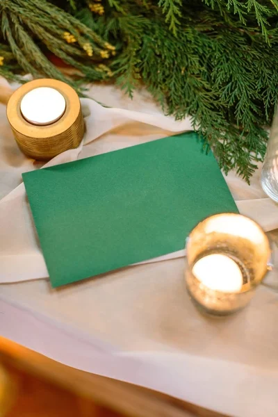 Background, wedding polygraphy, winter concept. misterious envelope of deep emerald colour is on the table covered with white silk drapping, burning candles are shining in the golden holders — Stock Photo, Image