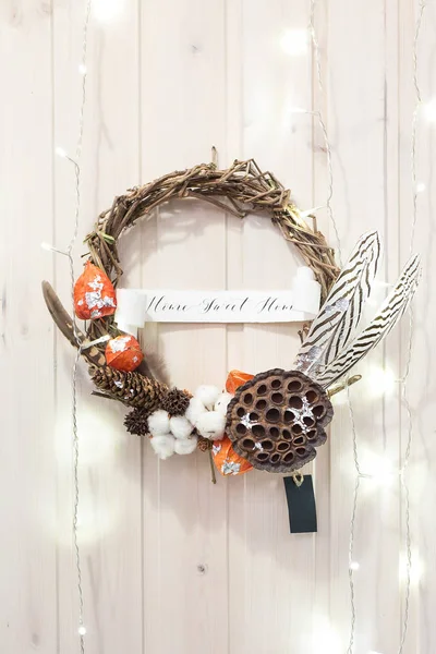 arts and crafts, creating, decor concept. wooden wall embellished with handmade wreath of perfect round form made of straws of some plants, of feathers and orange physalises, of cotton
