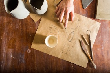 Çömlekçilik, heykel aletleri, seramik sanat konsepti - toprak malzemelerinin kalem çizimine yakın çekim, yığın dizayn ve mühendislikte usta el, tahta kahverengi masa üzerindeki kil bardaklar, üst görünüm