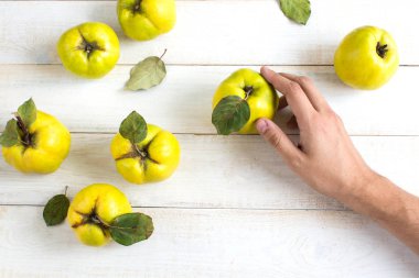 healthy food, nutrition, crop concept. top view of bright fine fruits with green leaves and dark hearts, they are placed on the white desk, and male hand is taking one of them clipart