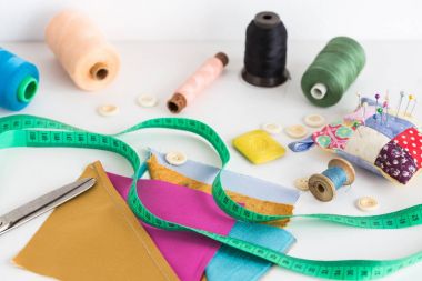 sabun dikiş araçları, patchwork, terzilik ve moda kavramı - closeup ölçme metre, iş parçacığı makaralar, iğnelik, düğmeler, makas, renkli patchwork kumaş parçaları ile beyaz masa,