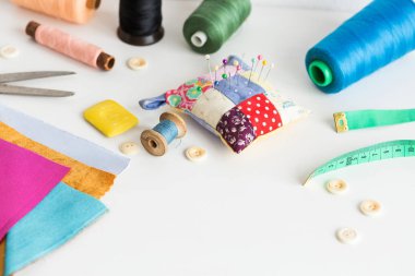 sabun dikiş araçları yakın çekim, patchwork, terzilik ve moda kavramı - çevre beyaz bir tablo, iş parçacığı makaralar, düğmeler, metre, iğnelik, makas, renkli patchwork kumaş parçaları üzerinde çalışma.