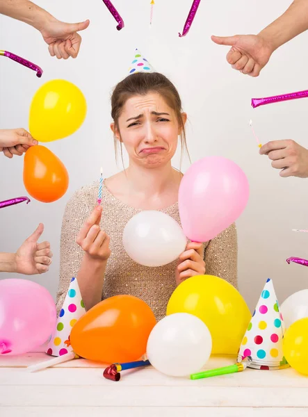 Fallar, sorpresa, concepto de aniversario. joven mujer caucásica con cabello oscuro está rodeada de globos y silbatos de cumpleaños, pero en su cara hay una mueca de tristeza, dolor y decepción —  Fotos de Stock